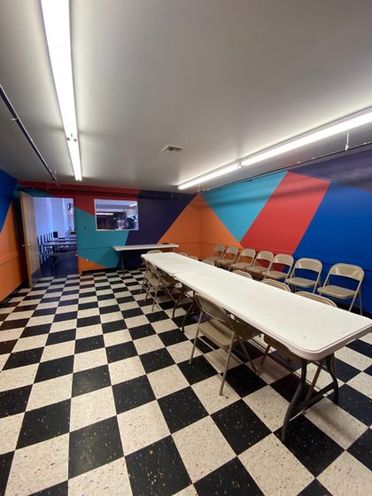 The Cake Room with long party tables, folding chairs and a bold color-block mural